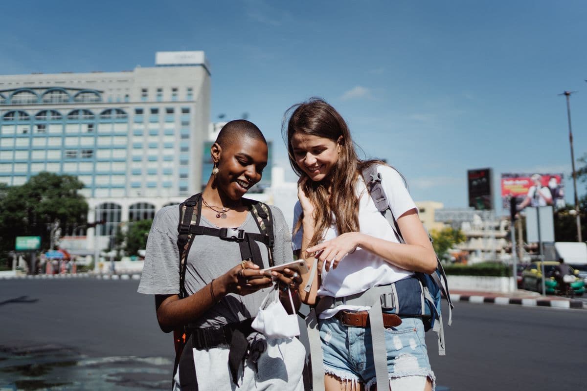 Two travellers with backpacks checking a phone on a sunny city street